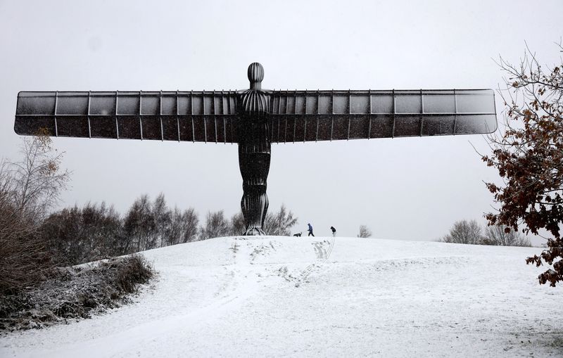 © Reuters. People walk their dog next to Antony Gormley's Angel of the North as snow continues to fall in Gateshead, Britain, November 23, 2024. REUTERS/Lee Smith