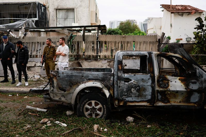 © Reuters. People gather at the scene where a projectile fell next to a destroyed vehicle, after projectiles crossed over to Israel from Lebanon, amid ongoing hostilities between Hezbollah and Israel, in Petah Tikva, Israel, November 24, 2024. REUTERS/Ammar Awad