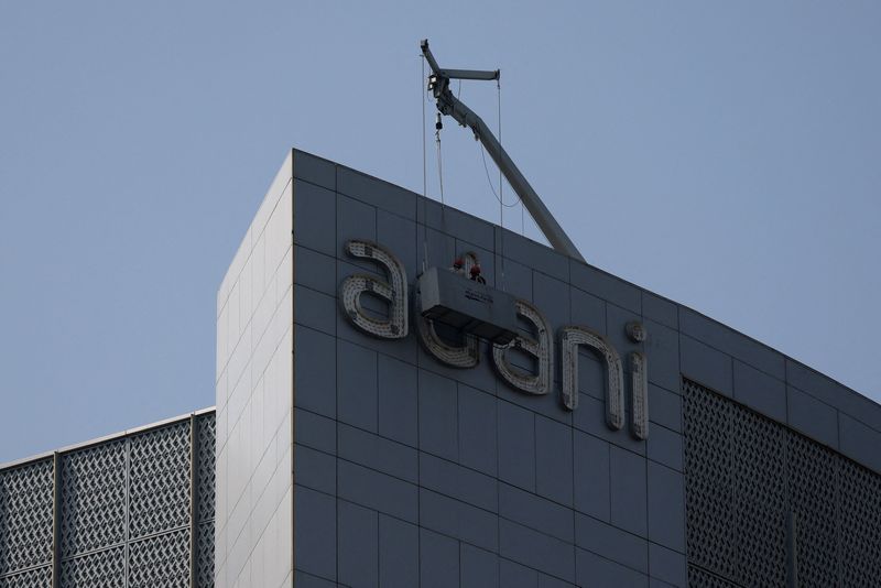 © Reuters. FILE PHOTO: Men fix the logo of the Adani Group on the facade of its Corporate House on the outskirts of Ahmedabad, India, November 21, 2024. REUTERS/Amit Dave/File Photo