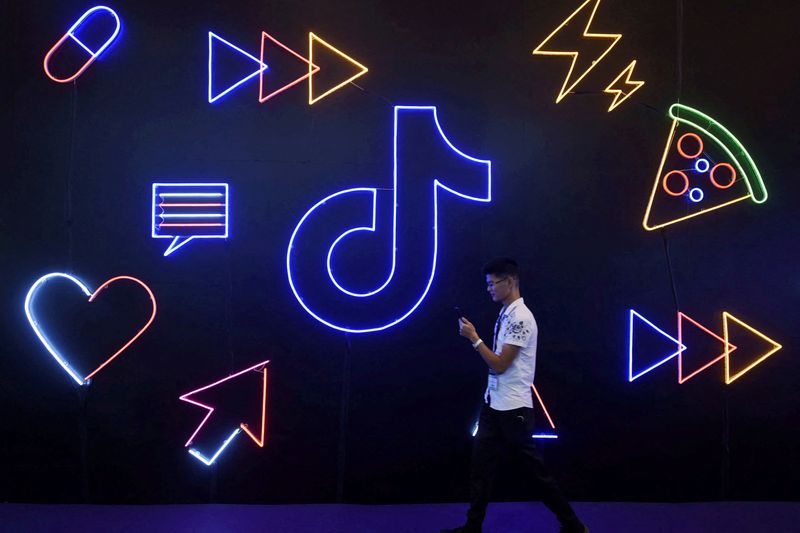 © Reuters. FILE PHOTO: A man holding a phone walks past a sign of Chinese company ByteDance's app TikTok, known locally as Douyin, at the International Artificial Products Expo in Hangzhou, Zhejiang province, China October 18, 2019. REUTERS/Stringer/File Photo