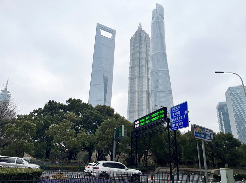 © Reuters. FILE PHOTO: Cars travel past a display showing Shanghai and Shenzhen stock indexes near the Shanghai Tower and other skyscrapers at the Lujiazui financial district in Shanghai, China February 5, 2024. REUTERS/Xihao Jiang/File Photo