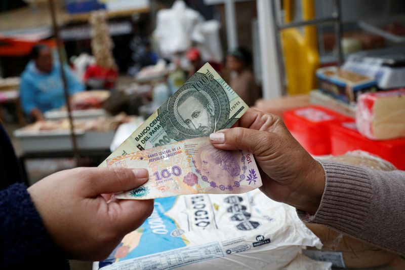 © Reuters. A customer and a salesperson pose for a photograph while holding Argentine and Paraguayan bills at a market near the border with Argentina, in Nanawa, Paraguay May 16, 2024. REUTERS/Cesar Olmedo/File Photo