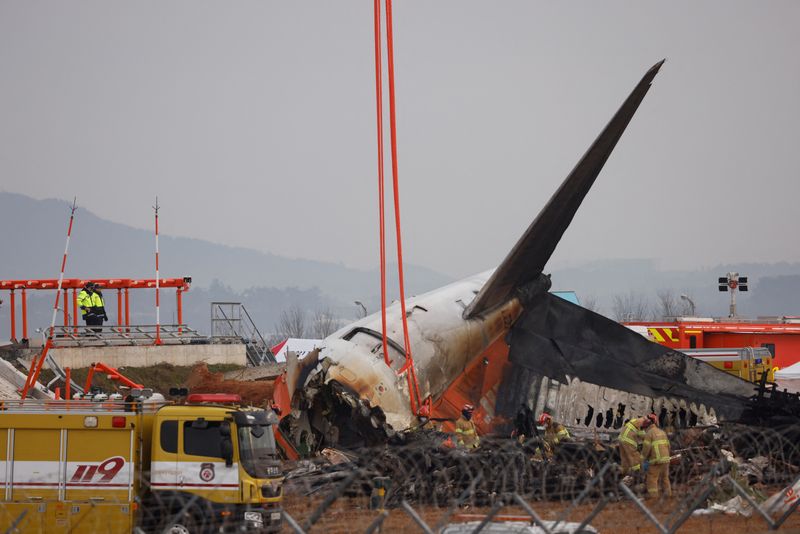 © Reuters. People stand as the wreckage of an aircraft lying on the ground after it went off the runway and crashed at Muan International Airport is pictured, in Muan, South Korea, December 30, 2024. REUTERS/Kim Soo-hyeon