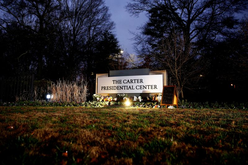 © Reuters. Flowers and mementos rest by the sign of The Carter Presidential Center, paying tribute to the life and legacy of former U.S. President Jimmy Carter, who passed away at the age of 100, in Atlanta, Georgia, U.S. December 30, 2024.  REUTERS/Octavio Jones