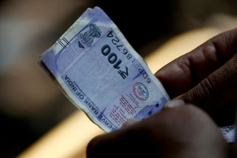 © Reuters. FILE PHOTO: A customer holds hundred rupees Indian currency notes near a roadside currency exchange stall in New Delhi, India, May 24, 2024. REUTERS/Priyanshu Singh/File Photo