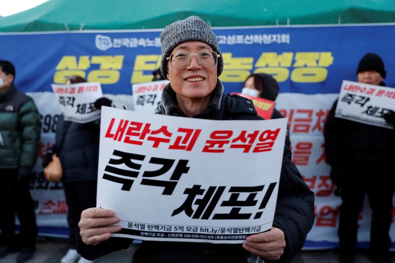 © Reuters. Lee Chul-woo, 70, who was tortured during the student democracy movement in the 80's and took part in rallies against the regime of former South Korean President Lee Myung-bak and Park Geun-hye, holds a banner that reads 'Bind Yoon Suk Yeol right now' during a rally to demand the resignation of South Korean President Yoon Suk Yeol, in Seoul, South Korea, December 6, 2024. REUTERS/Kim Soo-hyeon