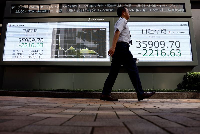 © Reuters. FILE PHOTO: A man walks past electronic screens displaying Japan's Nikkei share average outside a brokerage in Tokyo, Japan August 2, 2024. REUTERS/Issei Kato/File photo