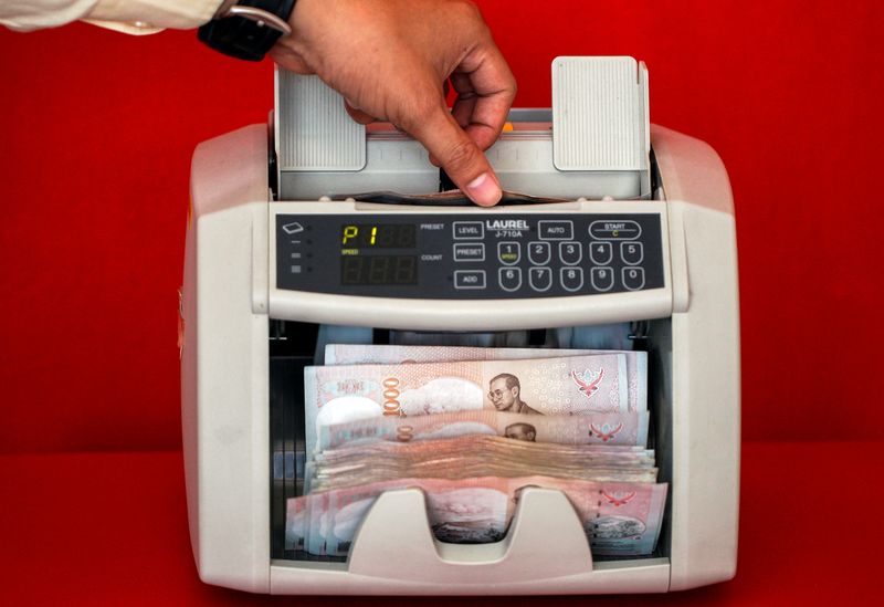 © Reuters. FILE PHOTO: A pawn shop worker uses a machine to count Thai Baht banknotes as he prepares to purchase items from customers at Easy Money Pawn shop in Bangkok, August 27, 2013.   REUTERS/Athit Perawongmetha/File Photo