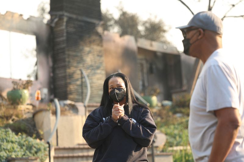 © Reuters. Inez Moore and her father Michael Moore stand near their burned family home after the Eaton Fire tore through a neighborhood, while a pair of massive wildfires menacing Los Angeles from the east and west were still burning uncontained, in Altadena, California, U.S. January 9, 2025. REUTERS/Mario Anzuoni