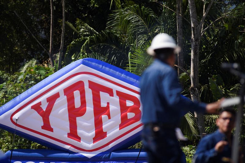 © Reuters. FILE PHOTO: The logo of Yacimientos Petrolíferos Fiscales Bolivianos (YPFB) is seen behind a worker at Mayaya Centro-X1, in Caranavi, Bolivia July 16, 2024. REUTERS/Claudia Morales/File Photo